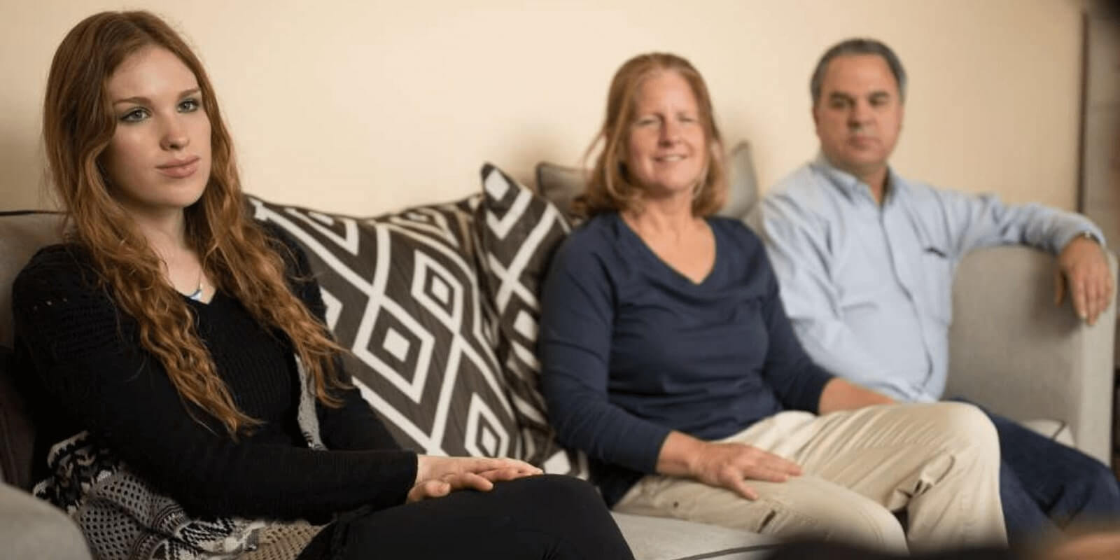 A teenage girl and her parents listening to therapist on a couch