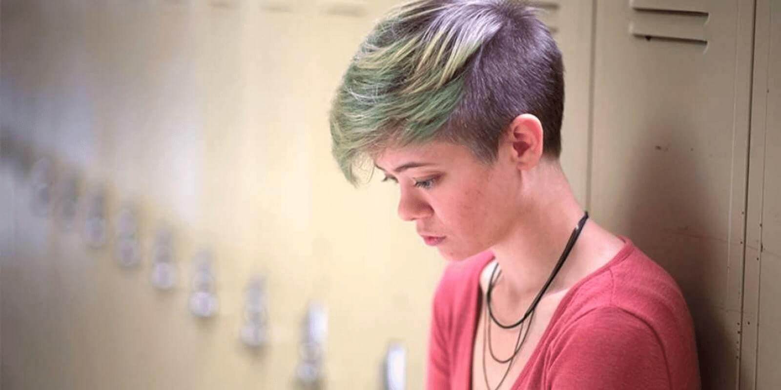 A high school student looking depressed in front of a locker