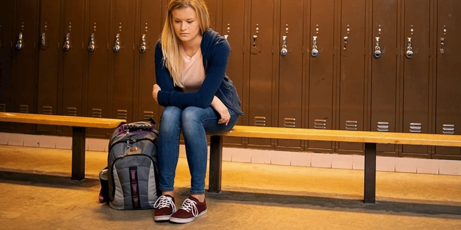 A teen girl sitting alone in the locker room sadly