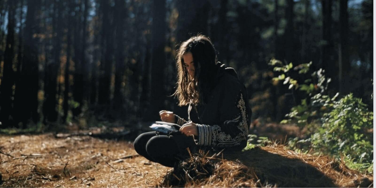 A girl holding cigarette in one hand and a bird on her lap in the woods