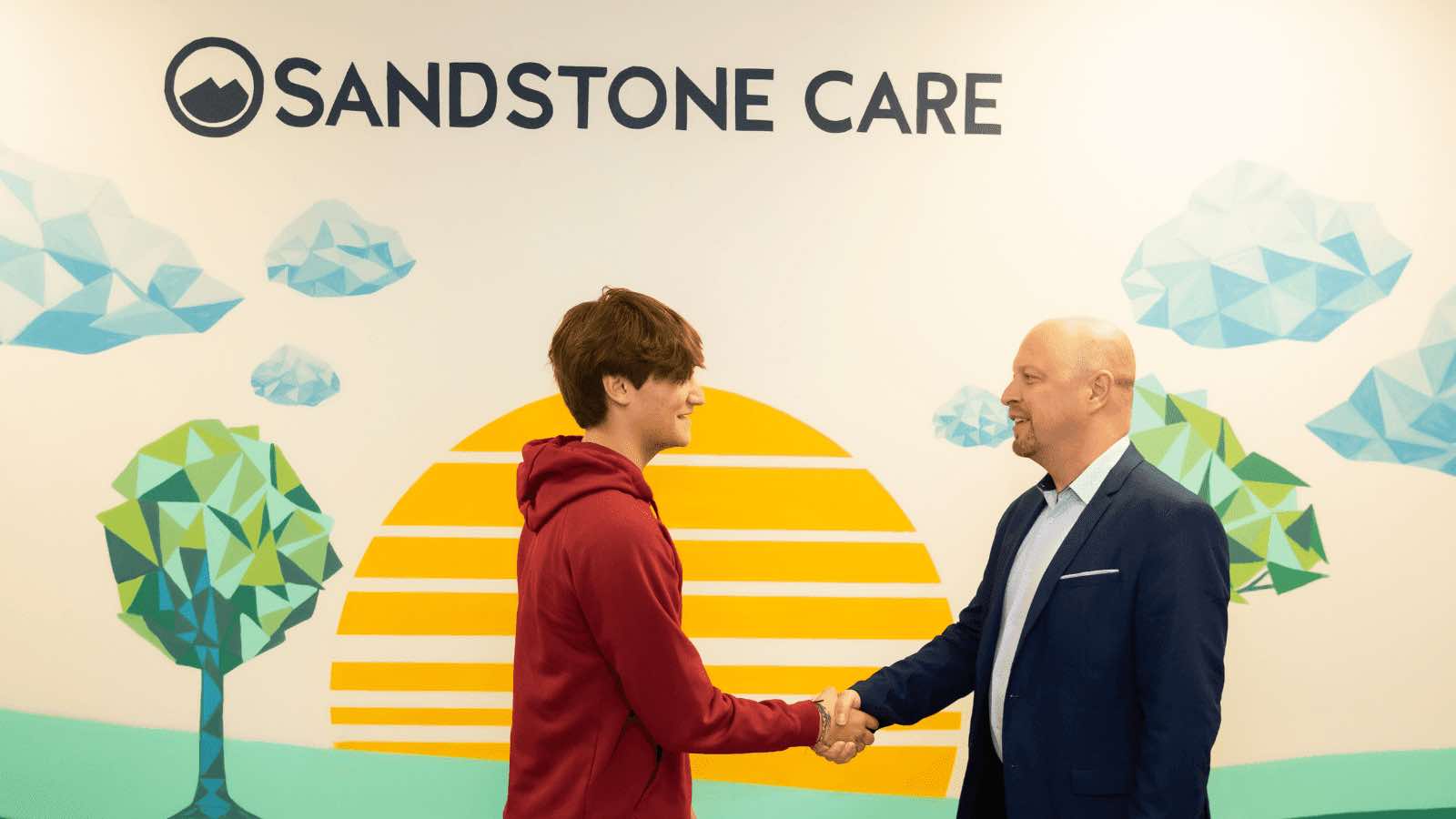 A Therapist welcoming a client in front of Buffalo Grove Rehab mural