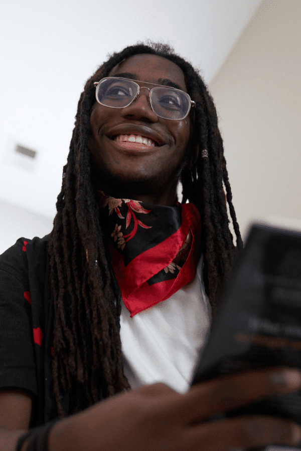smiling man with dreadlocks and glasses holding a cell phone