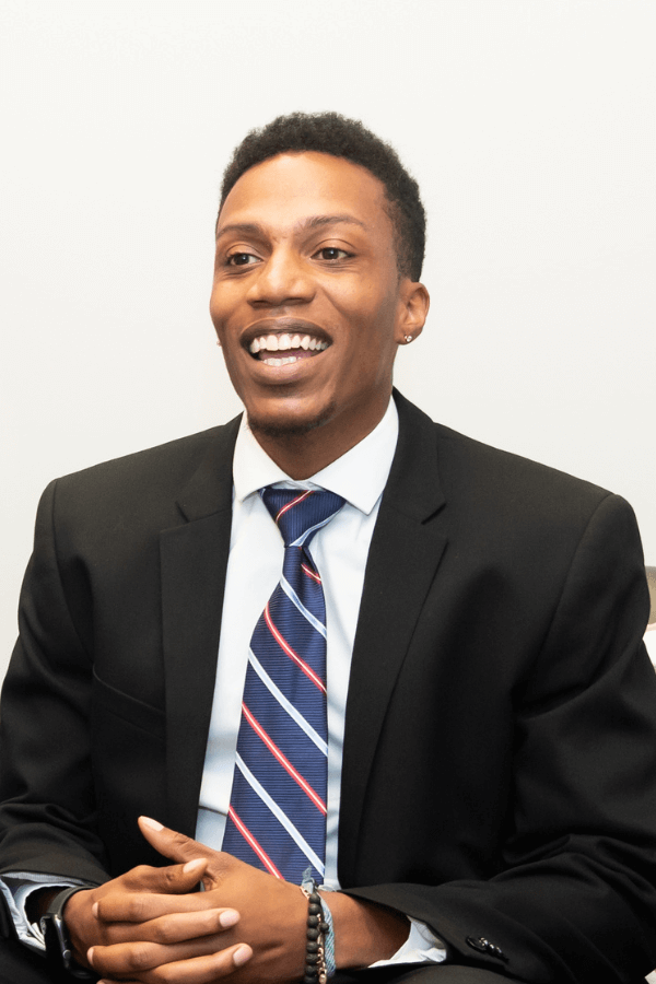 A young black man smiling in a suit.