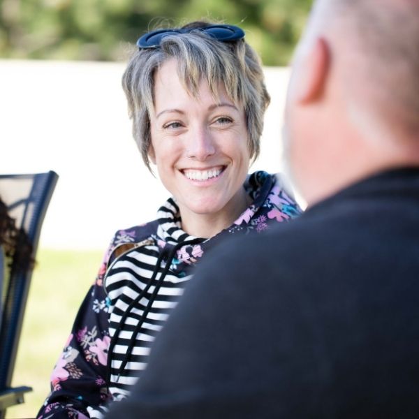 A middle-aged woman smiles at another client while they are outside.