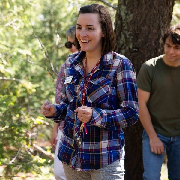Young woman with a nametag leading a hike in the woods.