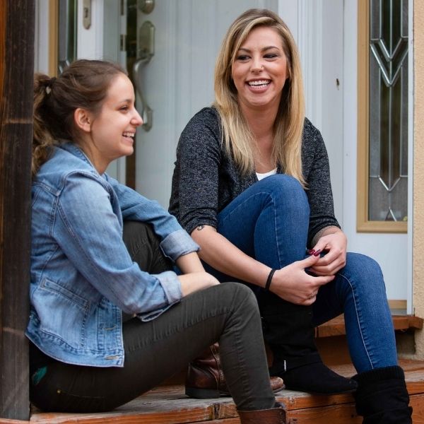 Two young women laughing while sitting on a porch.