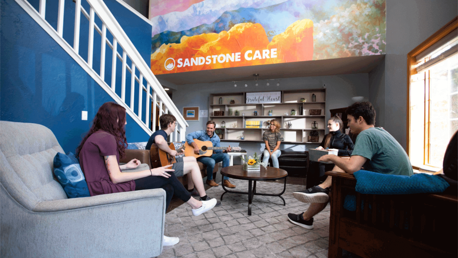 Group of young adults and their parents participating in a guitar music session in a rehab center