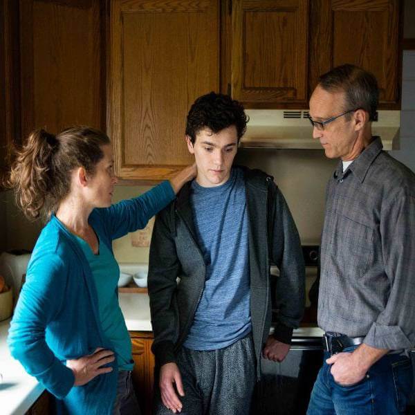 Parents in a kitchen comforting their teenage son.