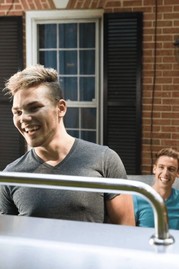 Two young men smiling at a house.