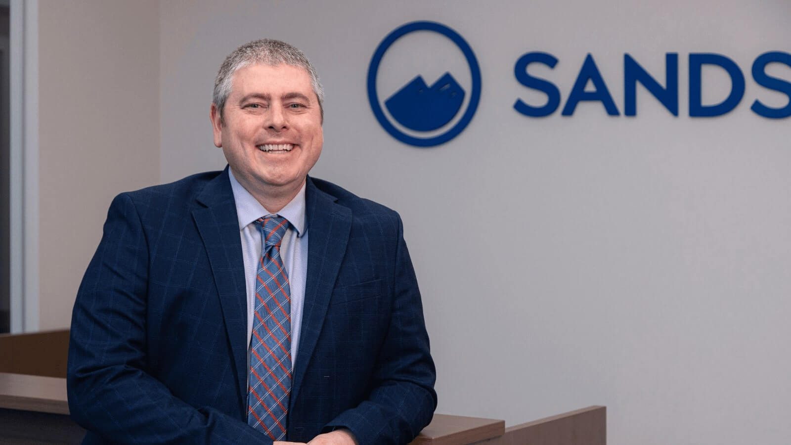 Dr. Osner smiling in front of a wall with Sandstone Care logo on it