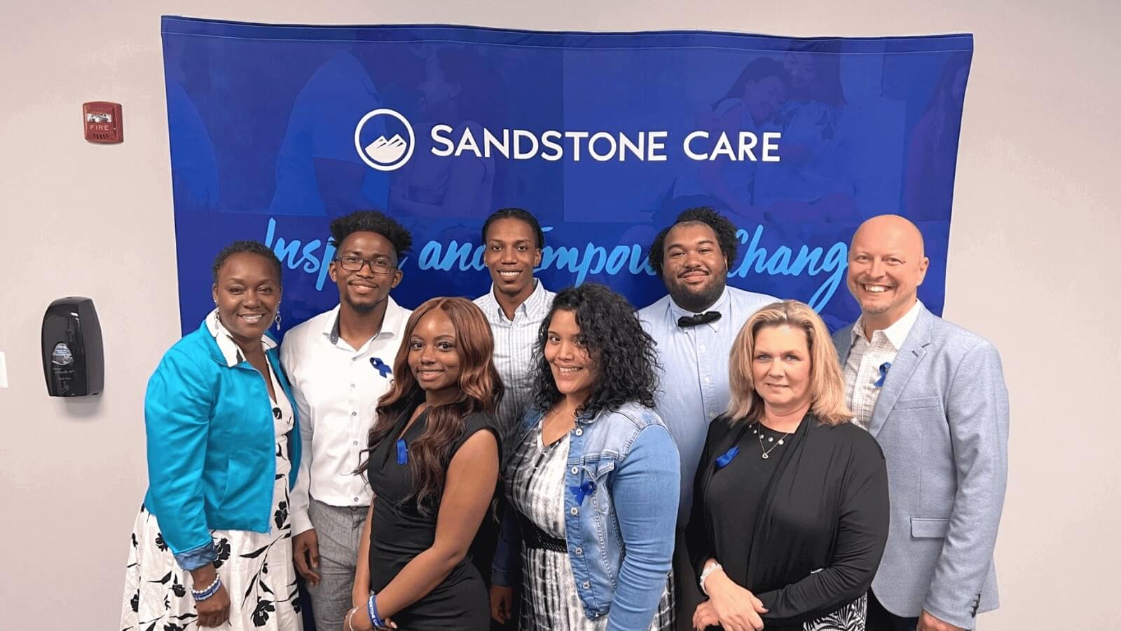 Sandstone Care Buffalo Grove team standing in front of Sandstone Care tapestry