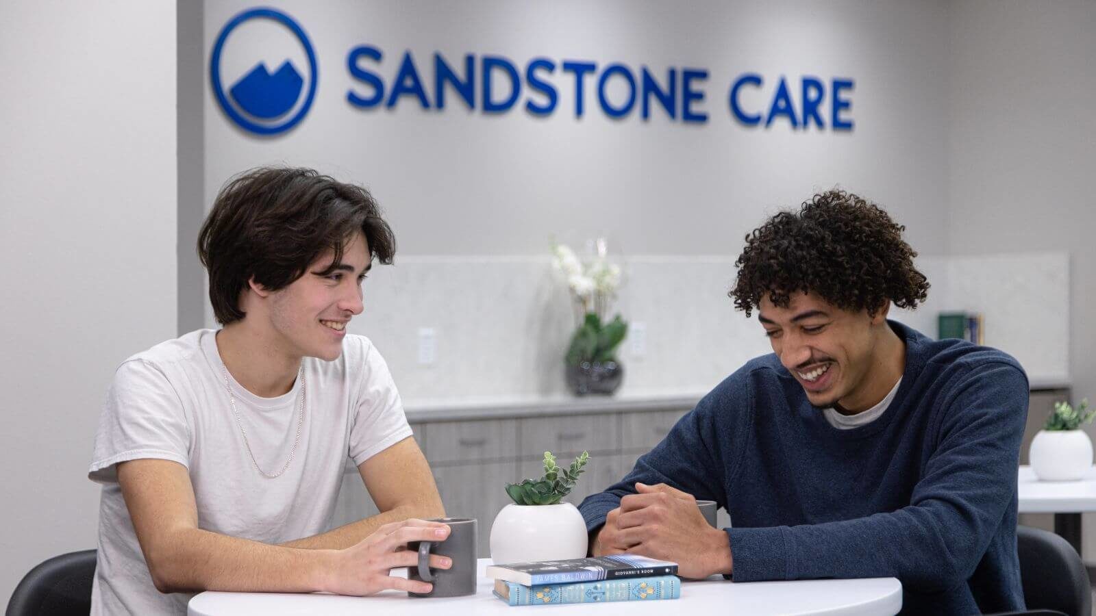 Two male clients talking to each other while sitting at a table in Sandstone Care Virginia Detox Center