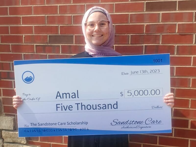 Amal - the 2023 sandstone care scholarship winner holding her $5,000 check