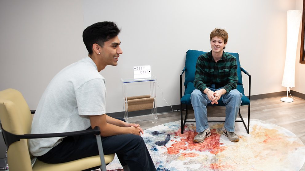 Two seated young adults smiling and talking in group discussion.