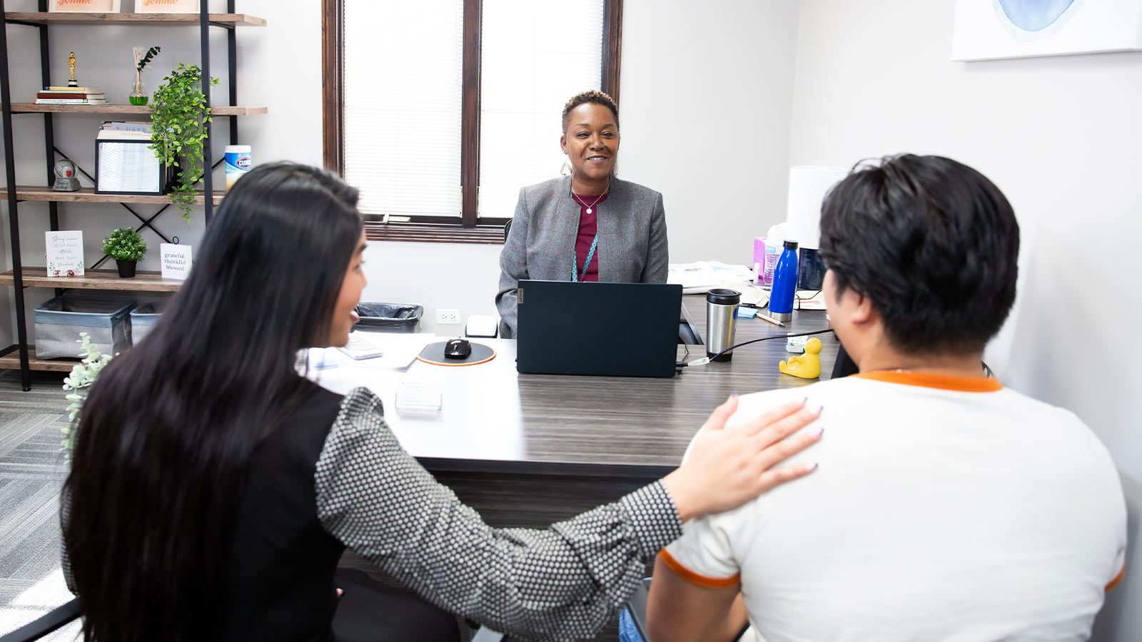 A professional talking to two people at her desk.